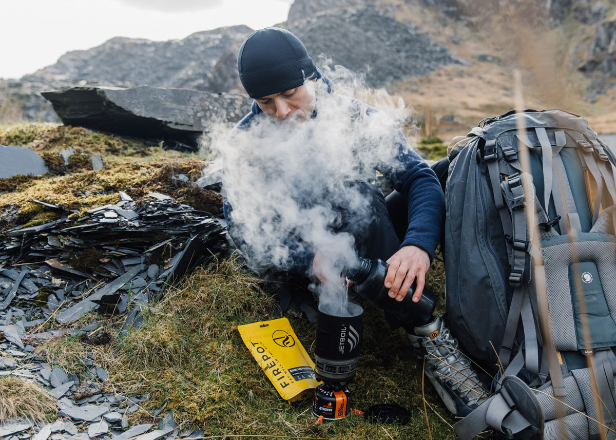 Turgåer lager mat på brenner i fjellet, med en gul Firepot-pose ved siden av